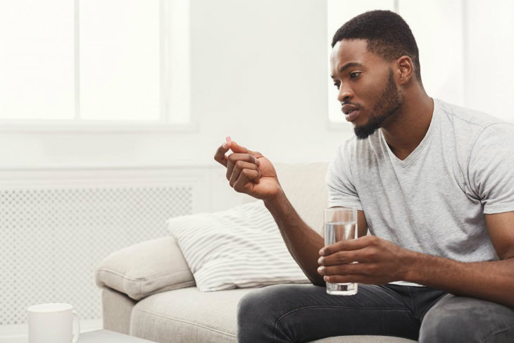 man-holding-glass-of-water-and-pill-of-anticids-taking-medication