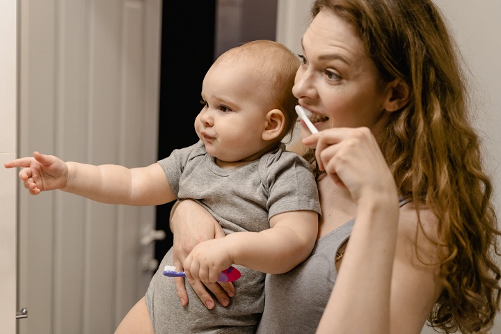 picture of a woman holding a baby in her hand and brushing her teeth