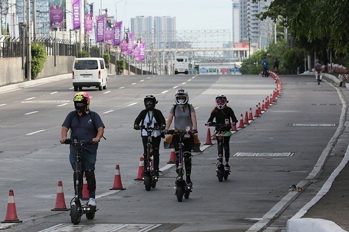 four people wearing protective gear while driving scooter on street