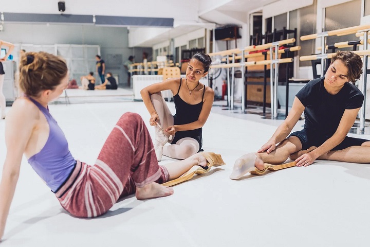 picture of ballerinas sitting on the ground of a dance studio with ballet foot stretchers