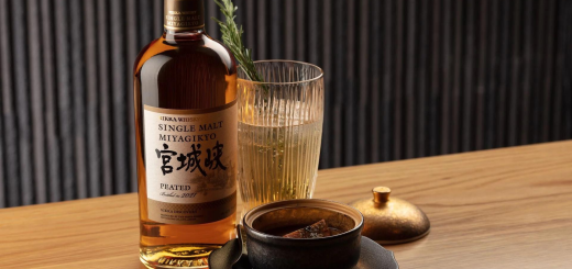 A bottle of Nikka Miyagikyo Peated Single Malt Whiskey beside a cocktail served in a glass mug.